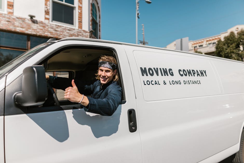 The image shows a white delivery van from Man with Van White City parked on a paved driveway, with the front facing the camera. The van is positioned beside a residential street with a row of houses,